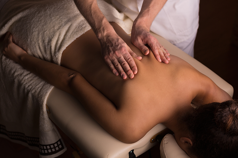 Masseur kneading the muscles on woman's back during therapeutic massage